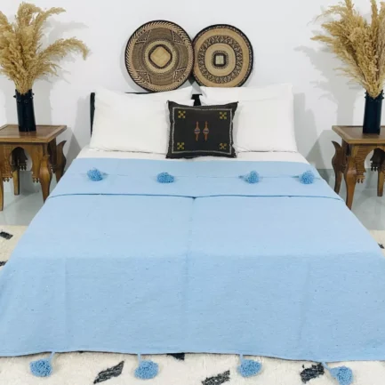 Handmade baby blue Moroccan pompom blanket displayed on a modern bed
