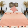Handmade Moroccan pompom blanket in solid salmon color, 100% cotton, displayed on a bed