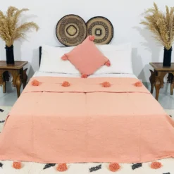 Handmade Moroccan pompom blanket in solid salmon color, 100% cotton, displayed on a bed