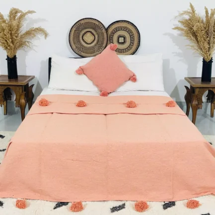 Handmade Moroccan pompom blanket in solid salmon color, 100% cotton, displayed on a bed