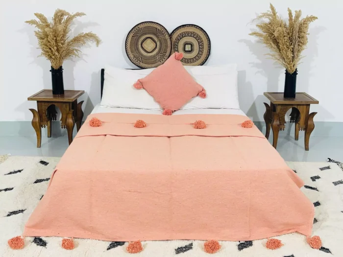 Handmade Moroccan pompom blanket in solid salmon color, 100% cotton, displayed on a bed