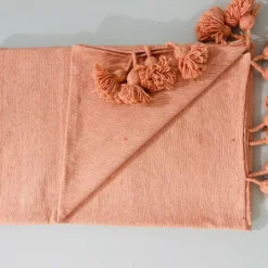 Folded Moroccan pompom blanket in salmon pink, made of soft cotton