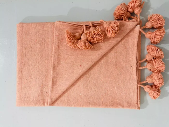 Folded Moroccan pompom blanket in salmon pink, made of soft cotton