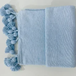 Light blue cotton throw blanket draped over a cozy neutral-toned sofa