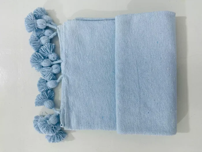 Light blue cotton throw blanket draped over a cozy neutral-toned sofa