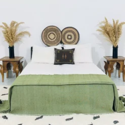 Olive green pompom blanket styled on bed in a cozy boho setting
