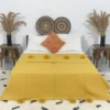 Handmade Moroccan pompom blanket in mustard yellow on bed