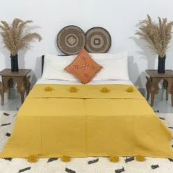 Handmade Moroccan pompom blanket in mustard yellow on bed
