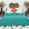 Handmade Moroccan pompom blanket in teal, styled on a bed