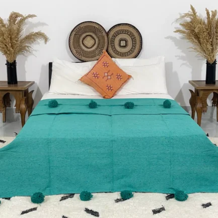 Handmade Moroccan pompom blanket in teal, styled on a bed
