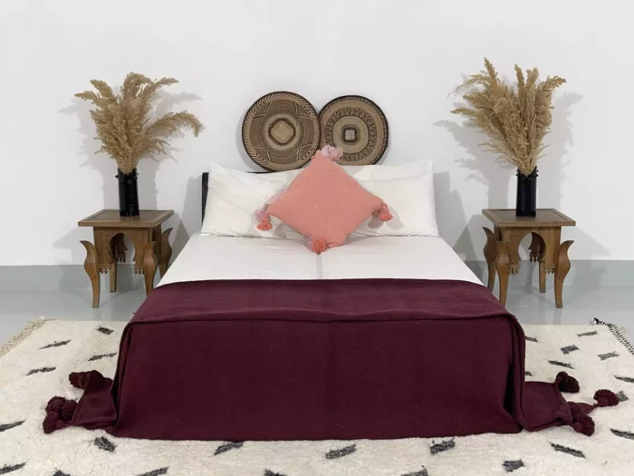 Moroccan burgundy pompom blanket styled in a bohemian bedroom setting