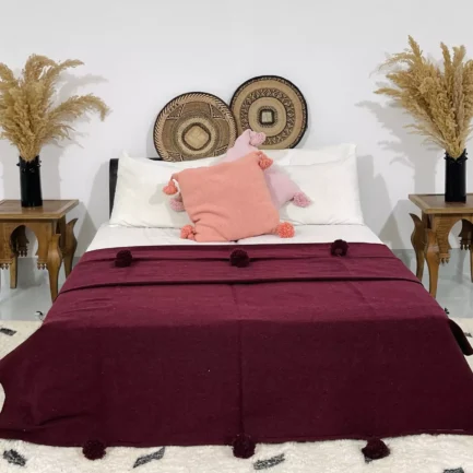 Handmade Moroccan pompom blanket in burgundy on a bed