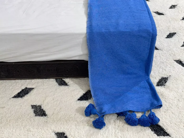 Label tag showing 100% cotton material on royal blue pompom blanket