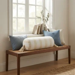 Cream and white striped bolster pillow with tassels styled on a wooden window bench