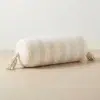 Cream and white striped cylindrical bolster pillow cover with tassels on a neutral background