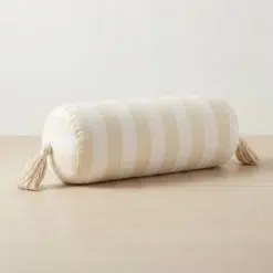 Cream and white striped cylindrical bolster pillow cover with tassels on a neutral background