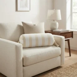 Cream and white striped bolster pillow with tassels styled on a neutral armchair