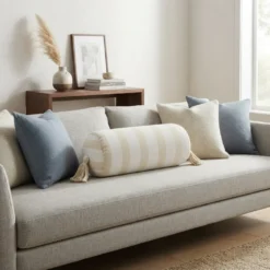Cream and white striped bolster pillow with tassels styled on a neutral sofa