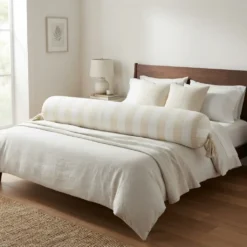 Extra long cream and white striped bolster pillow across a neutral bed