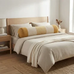 Extra long bolster pillow styled across a neutral bed with handcrafted tassels