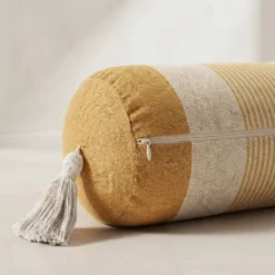 Close-up of mustard and ivory striped bolster pillow showing concealed zipper and tassel