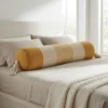 Mustard and ivory striped bolster pillow with tassels styled on a neutral bed