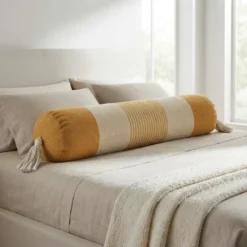 Mustard and ivory striped bolster pillow with tassels styled on a neutral bed