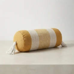 Mustard and ivory striped bolster pillow with tassels styled in a neutral living room