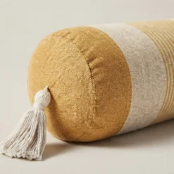 Mustard and ivory striped cylindrical bolster pillow cover with tassels on a neutral background