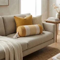 Mustard and ivory striped bolster pillow with tassels styled on a neutral sofa